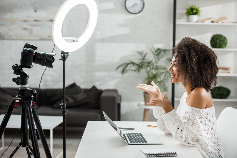 Produtora de conteúdo gravando um vídeo em uma sala com decoração branca, usando uma câmera e ring light