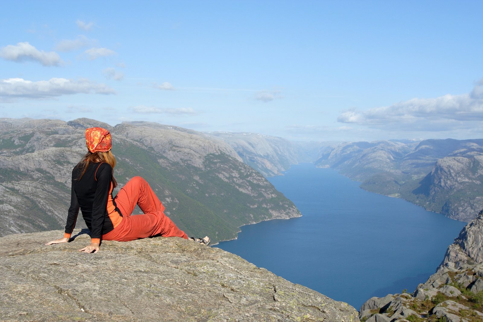 mulher sentada em pedra no penhasco, admirando a paisagem de rio e montanhas