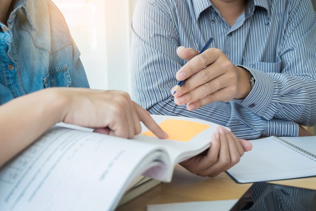 duas pessoas estudando juntas em uma mesa com muitos livros