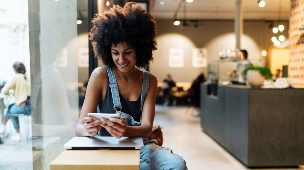 moça sentada em restaurante sorrindo enquanto olha para o celular