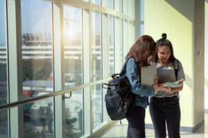 duas adolescentes lendo uma apostila ao lado de vidraça com vista da cidade